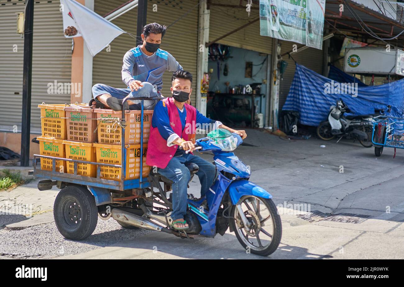 Employés sur un marché des fruits et légumes en Thaïlande, transportant des boîtes de fruits sur une moto. Banque D'Images