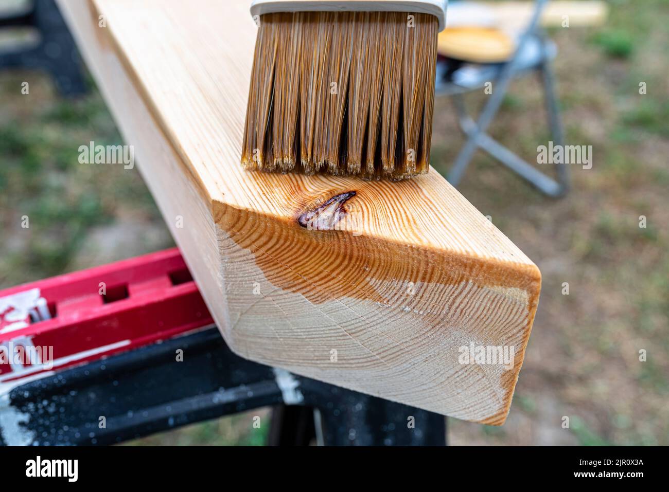 La femme imprègne des poutres de pin en bois rabotées avec des dimensions de 100x100mm avec une imprégnation incolore. Banque D'Images