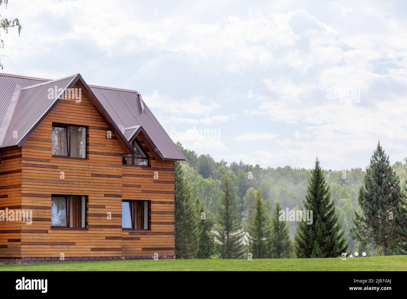 Cottage en bois de deux étages avec fenêtres nature et pelouse verte. Vente ou achat de maisons neuves. Un hôtel pour les touristes. Banque D'Images