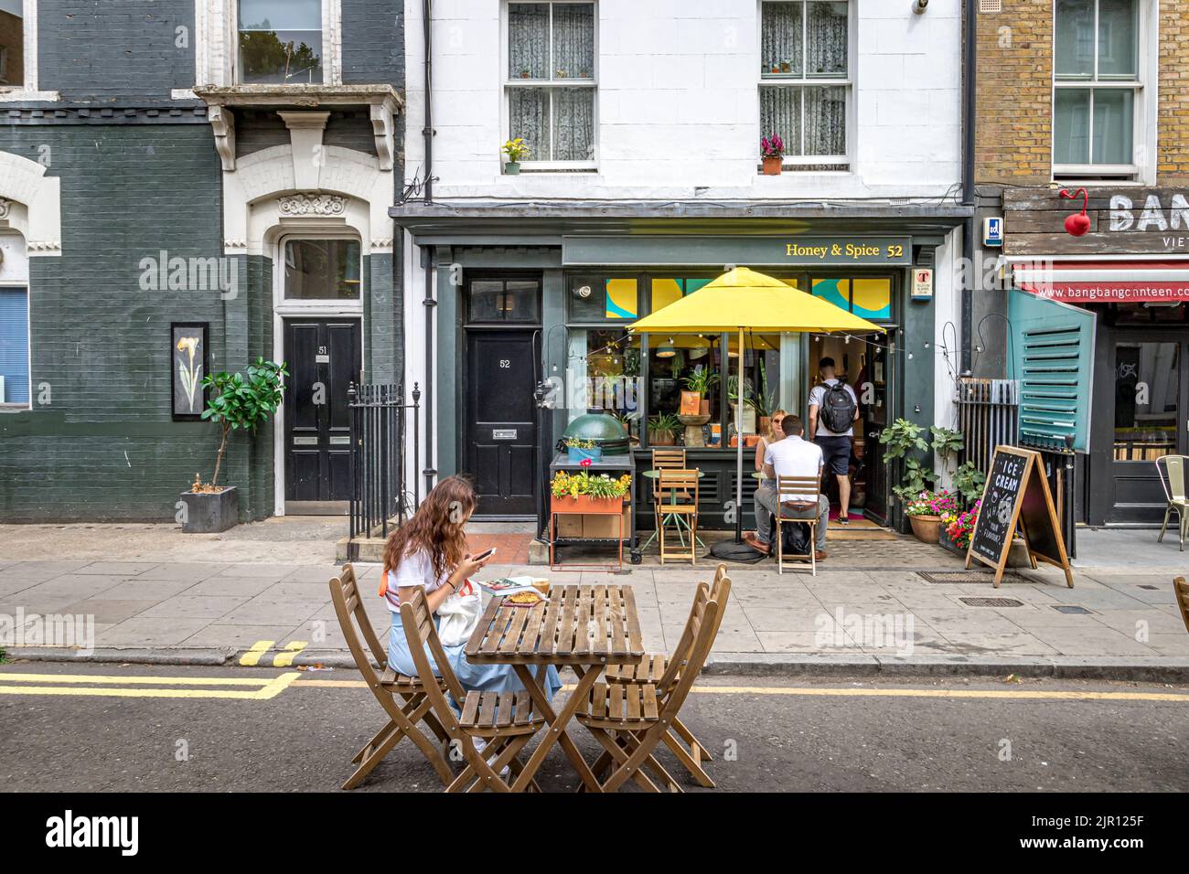 Une jeune femme assise et regardant son téléphone mobile à l'extérieur de Honey & Spice sur Warren Street , Londres W1 Banque D'Images