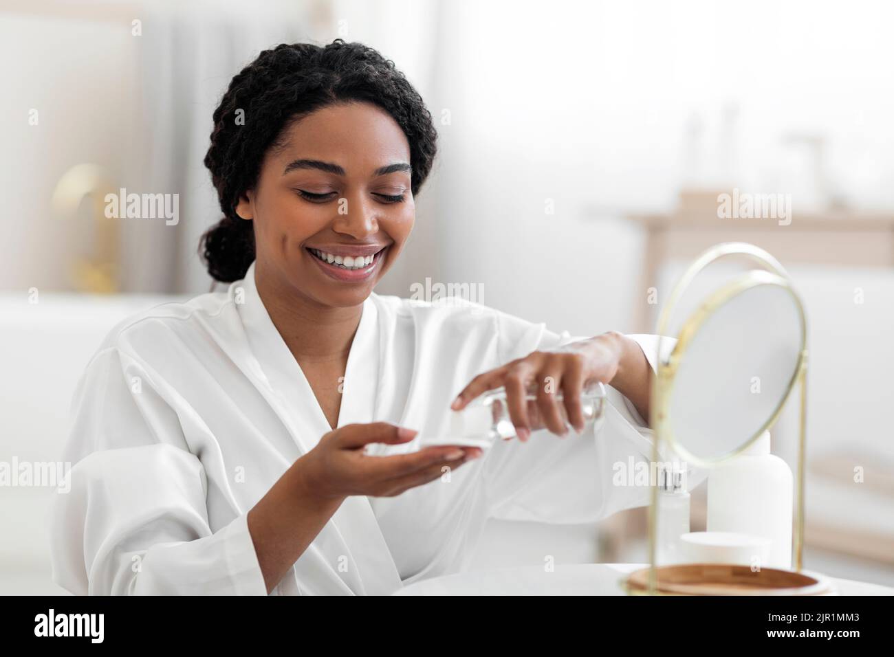Femme noire souriante utilisant un tampon de coton et de l'eau micellaire pour les soins de la peau Banque D'Images