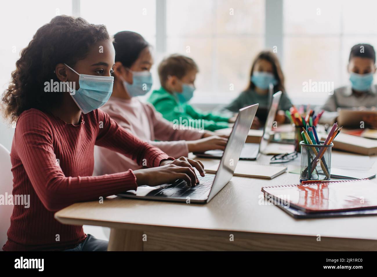 Divers enfants de l'école utilisant des ordinateurs portant des masques faciaux en classe Banque D'Images