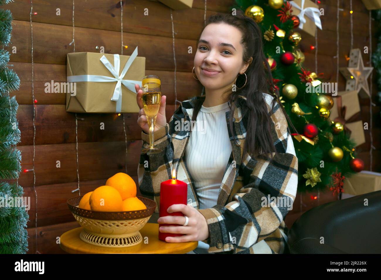 Fille dans des vêtements décontractés avec un verre de champagne près de l'arbre de Noël. Banque D'Images