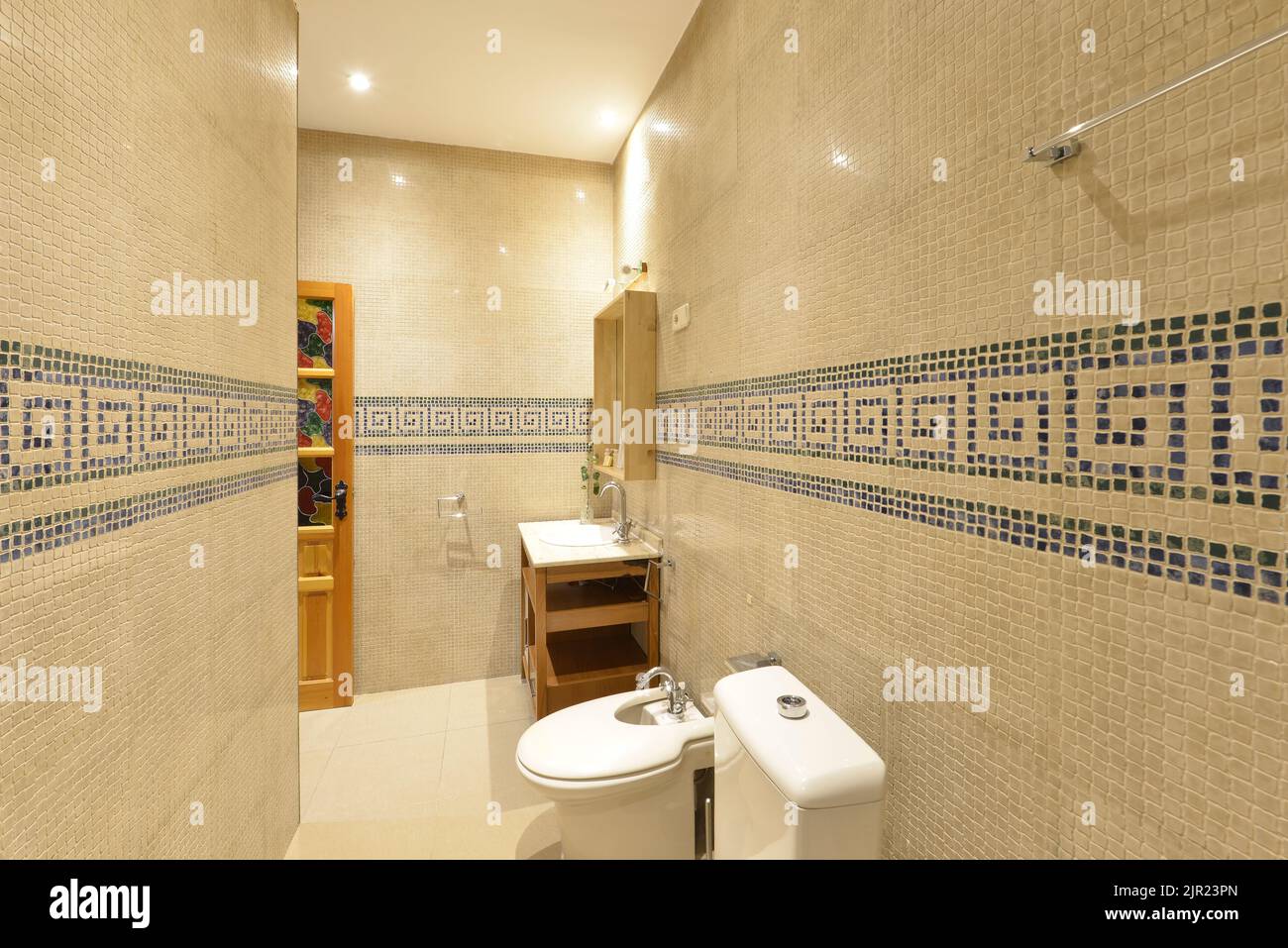 Salle de bains avec évier en porcelaine blanche, armoire en bois ouverte, miroir avec cadre assorti et carreaux de mosaïque avec bordure bleue Banque D'Images