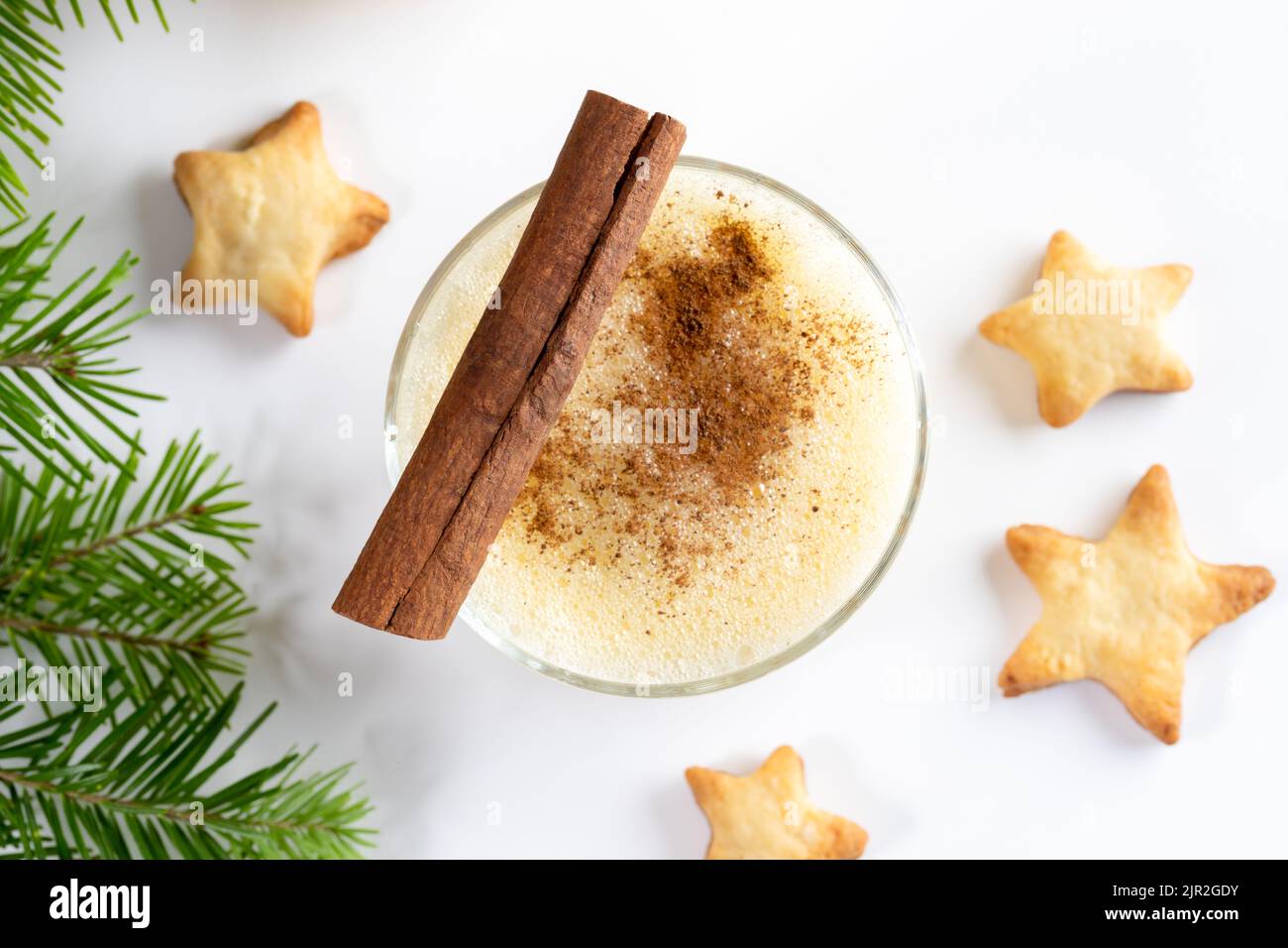 Cadeau de Noël traditionnel. Verre de lait de poule maison avec bâton de cannelle, biscuits de Noël étoiles, branches de sapin sur fond blanc. Vue de dessus. Clos Banque D'Images