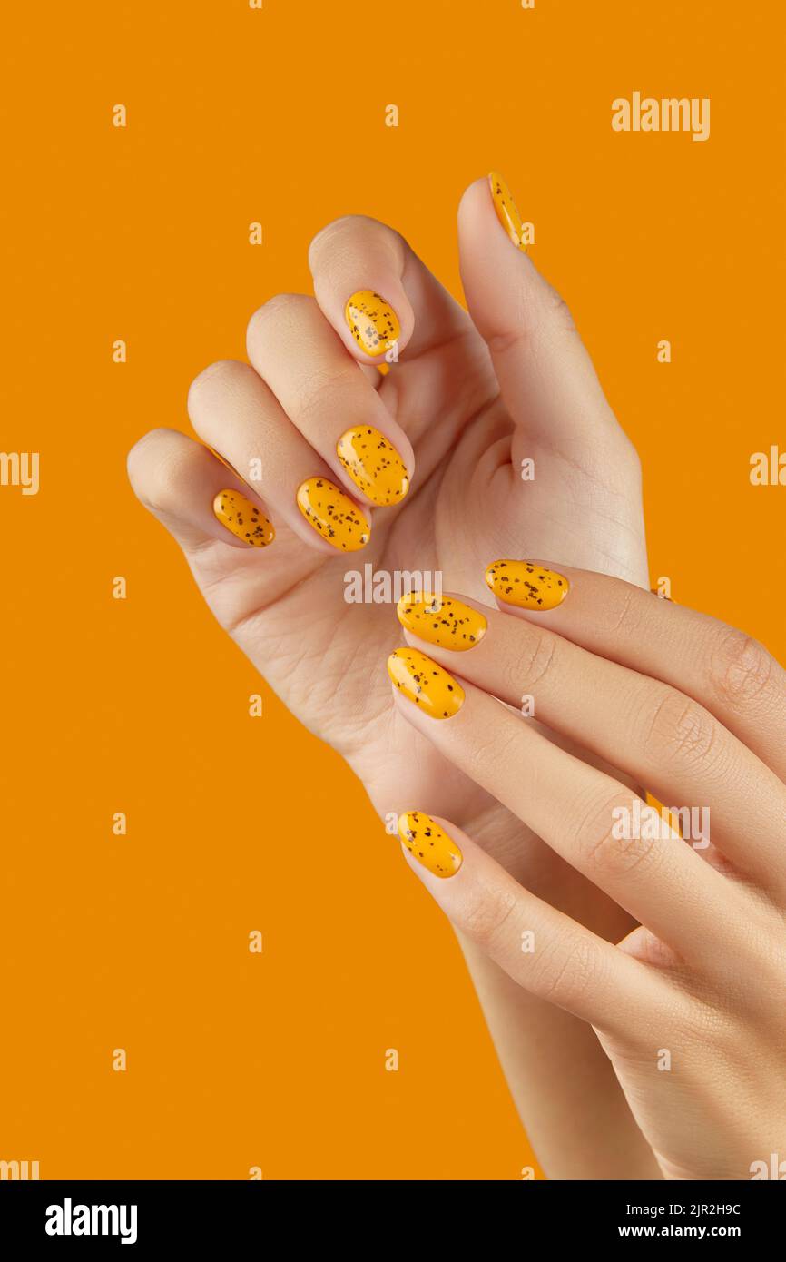 Des mains de femmes soignées avec un motif à ongles tendance sur fond orange Banque D'Images