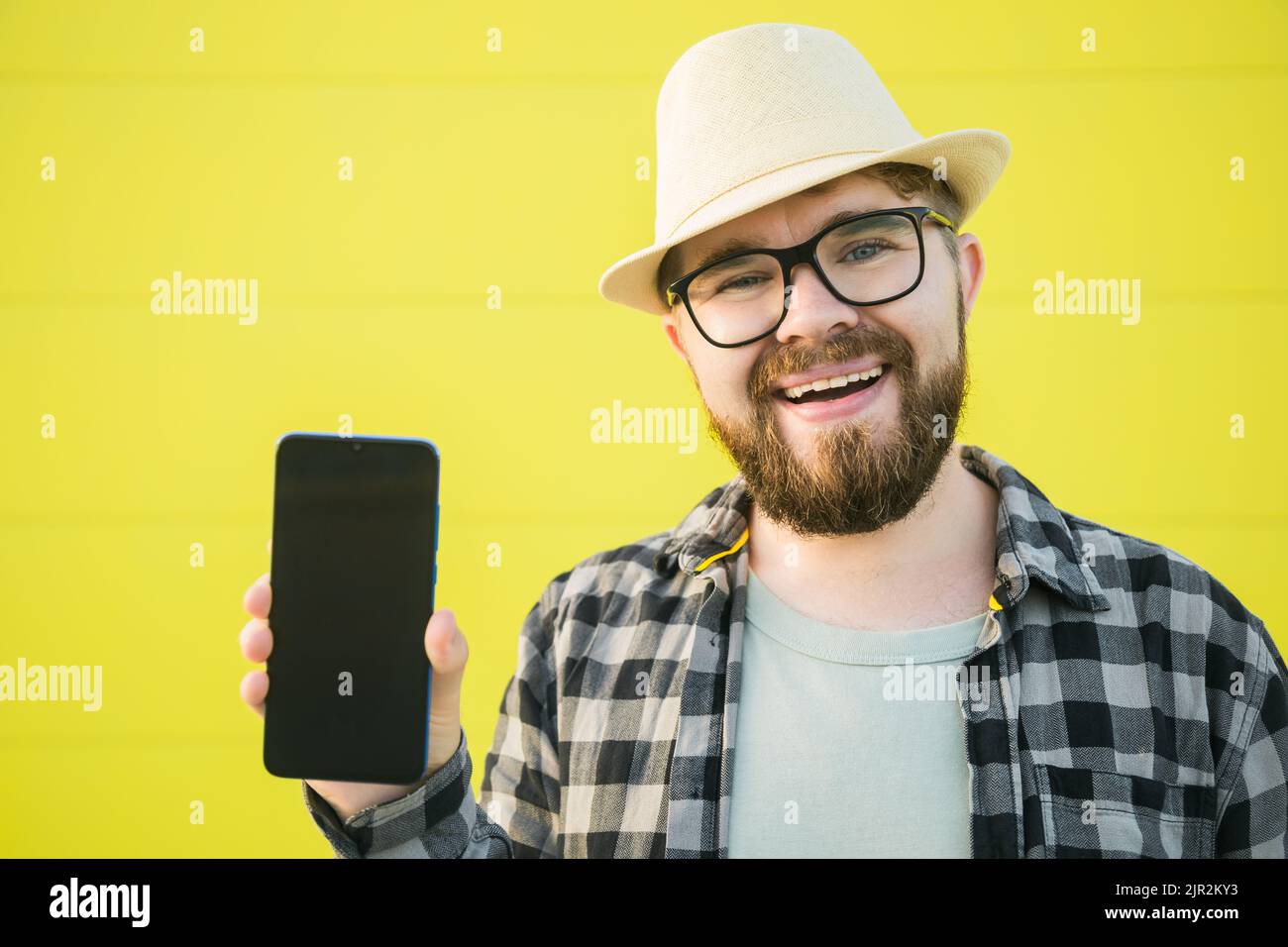 Joyeux sourire barbu porter chapeau homme montrant le téléphone mobile sur fond jaune - espace vide et endroit pour la publicité Banque D'Images