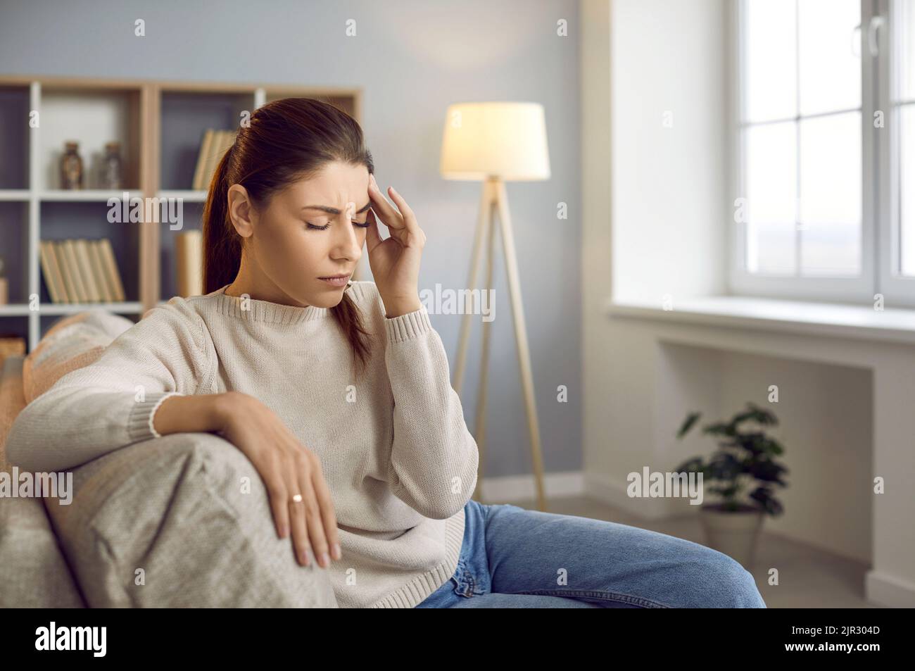 Une femme stressée et fatiguée qui a un mal de tête sévère est assise sur le canapé à la maison Banque D'Images