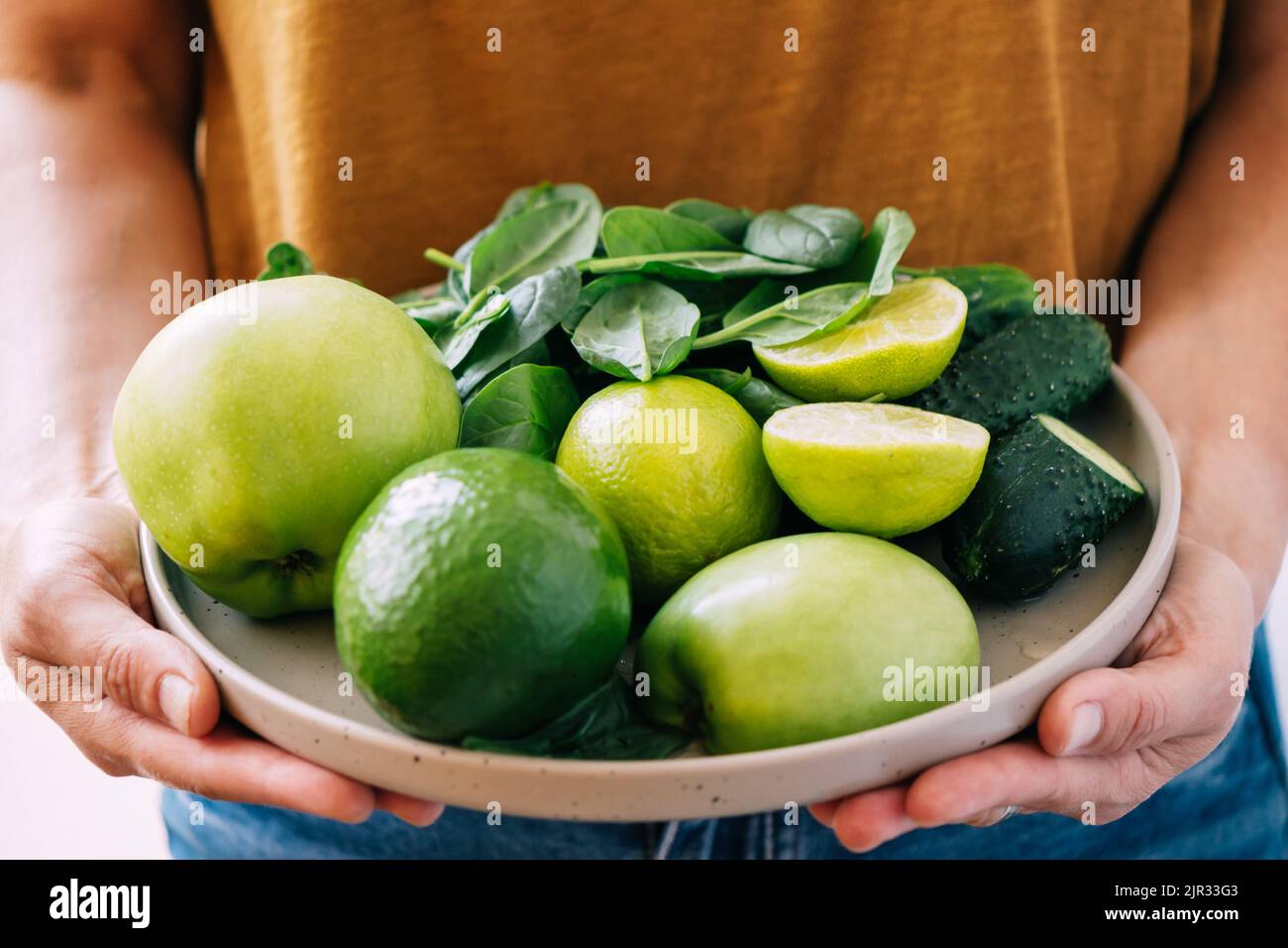 Une femme tient dans ses mains des légumes et des fruits verts frais dans une grande assiette, gros plan de mise au point douce Banque D'Images