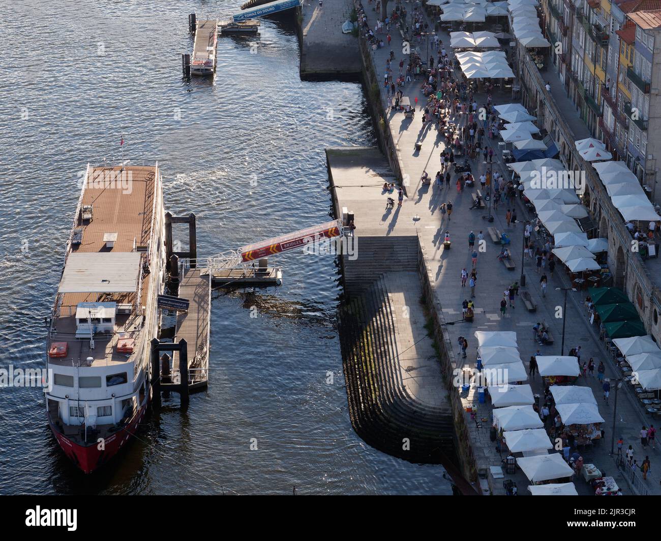 Ribeira quartier de Porto Portugal d'en haut avec un bateau amarré sur le fleuve douro. Les gens marchent le long de la promenade parmi les étals du marché. Banque D'Images