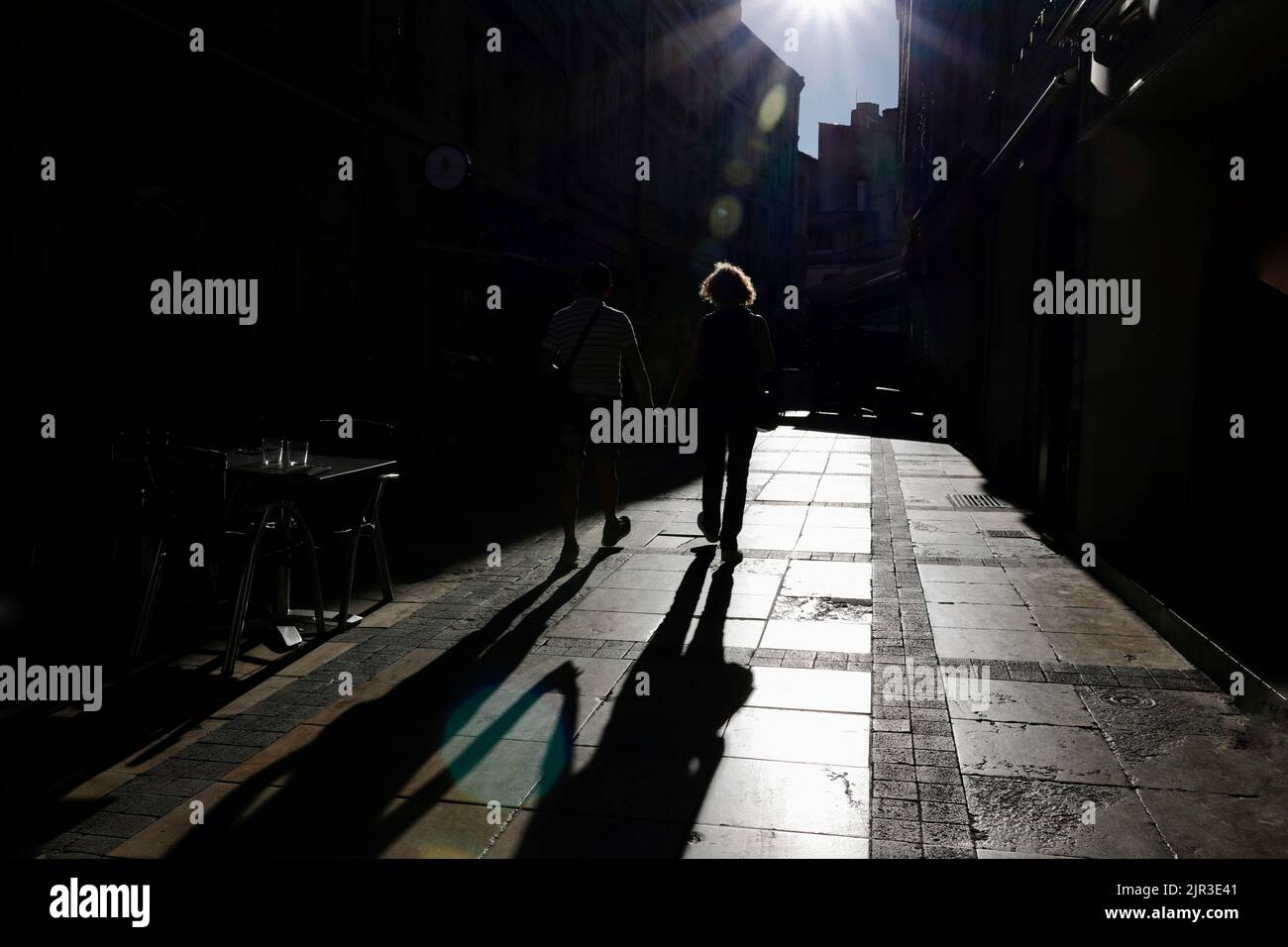 Un couple tenant les mains comme ils marchent au soleil, jetant une longue ombre sur la rue Banque D'Images