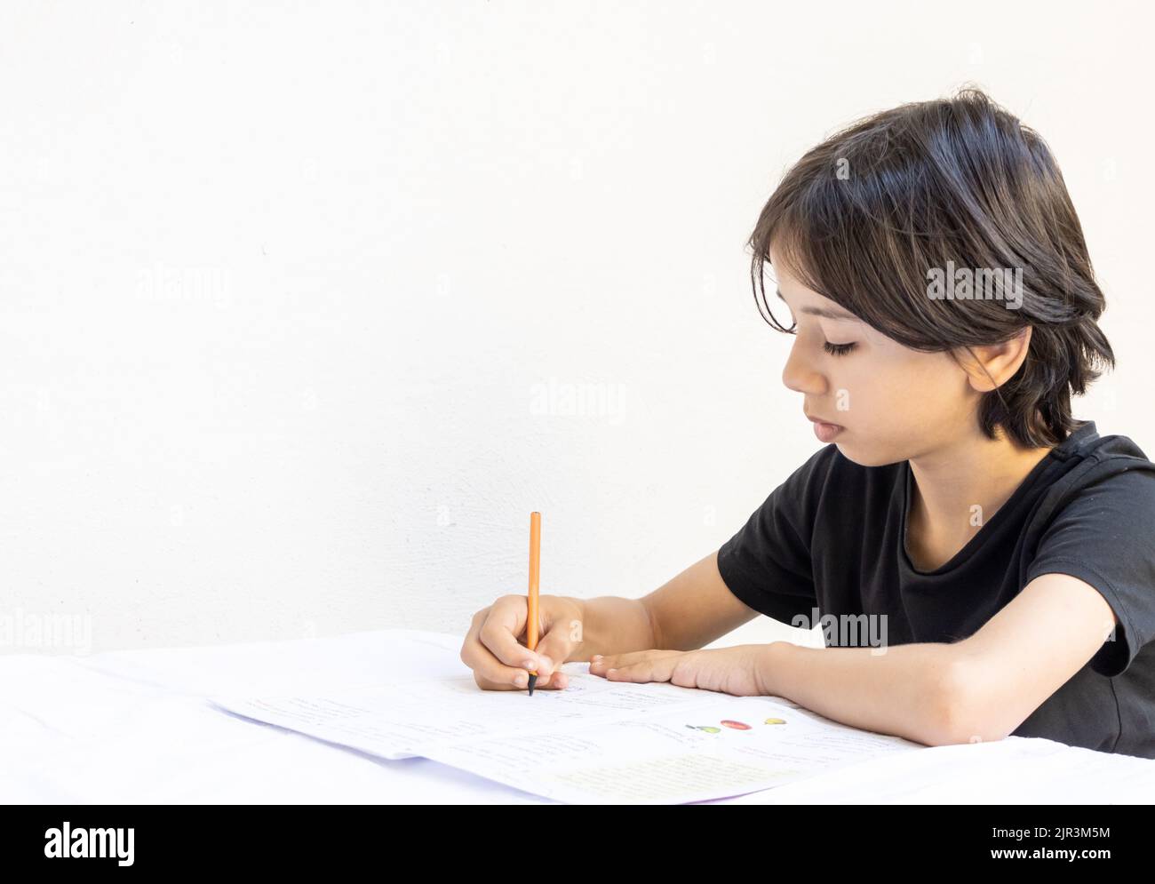 Un jeune adolescent d'asie de l'est étudie l'écriture avec un stylo et un carnet à la table. Le garçon qui fait ses devoirs à l'école à la maison. T-shirt noir Banque D'Images