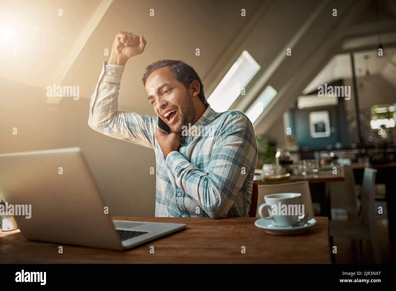 Profitez des opportunités qui s'offrent à vous. Un jeune homme parle sur son téléphone tout en utilisant son ordinateur portable. Banque D'Images