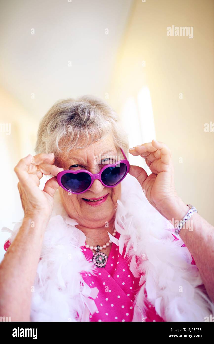 Le rose est et sera toujours ma couleur préférée. Une femme âgée insouciante mettant des lunettes roses à l'intérieur d'un bâtiment. Banque D'Images