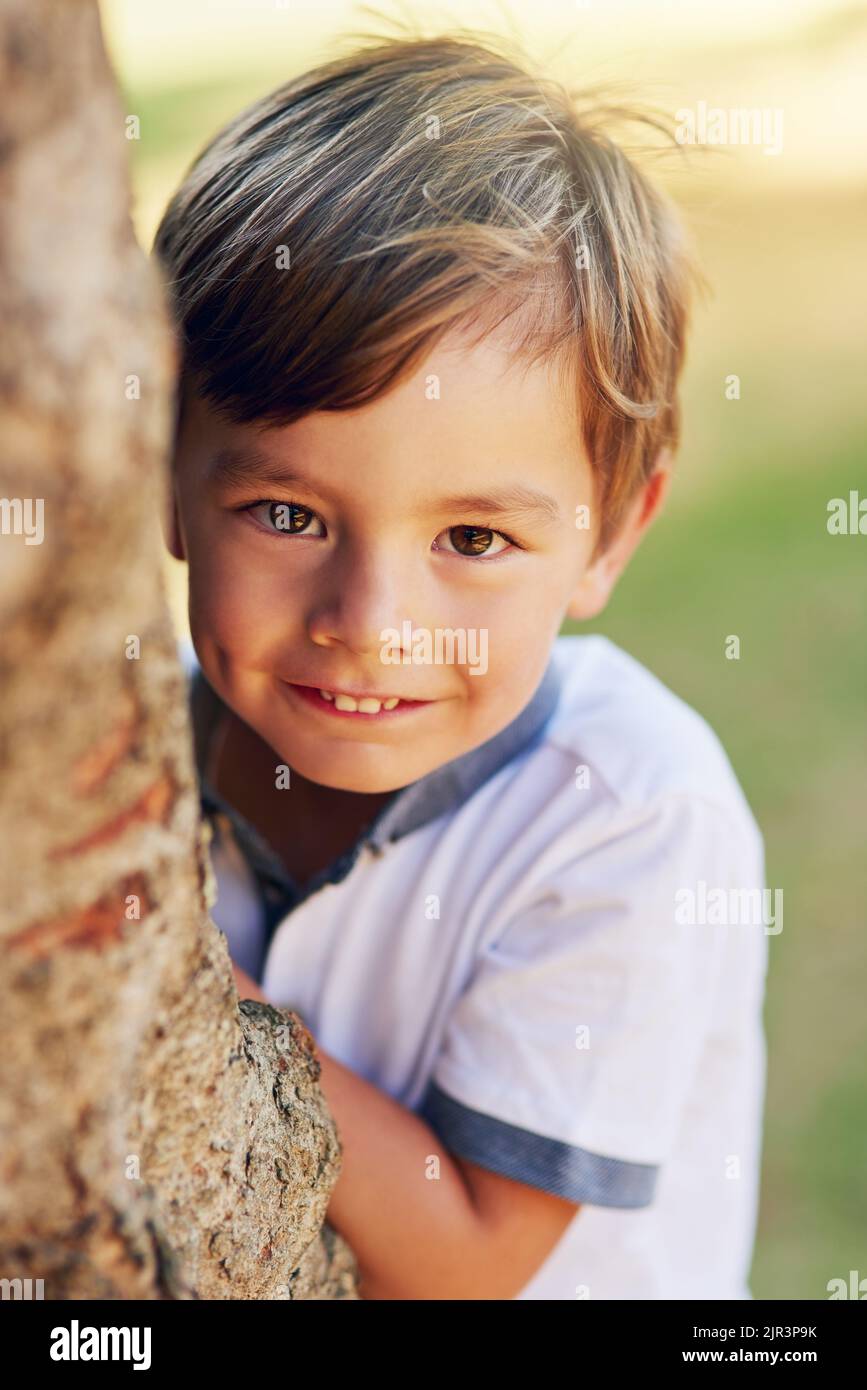 Le summum de l'enfance - cacher et chercher. Un petit garçon heureux jouant à côté d'un arbre dans le parc. Banque D'Images