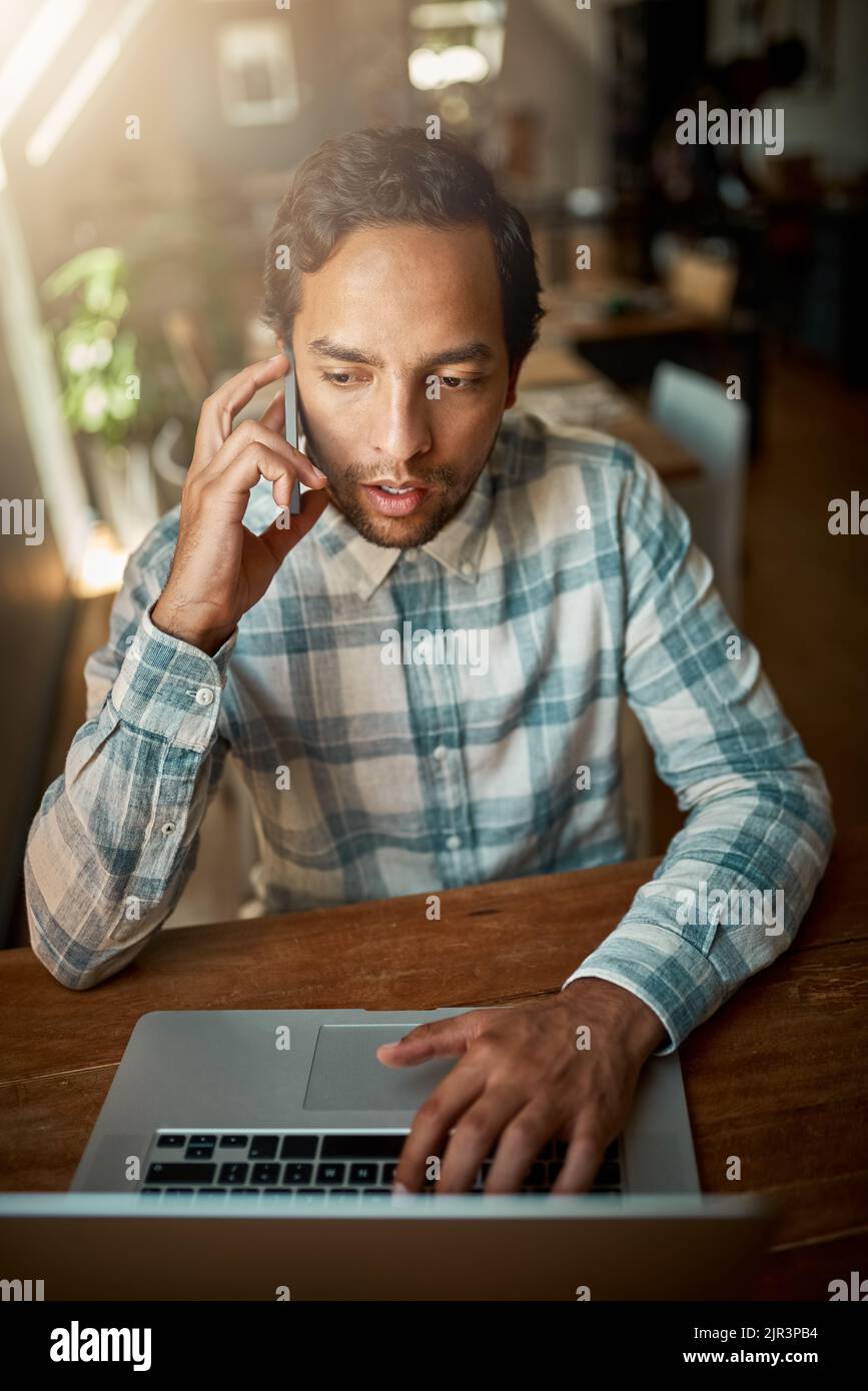 Il est toujours temps pour les affaires. Un jeune homme parlant sur son téléphone tout en utilisant son ordinateur portable. Banque D'Images