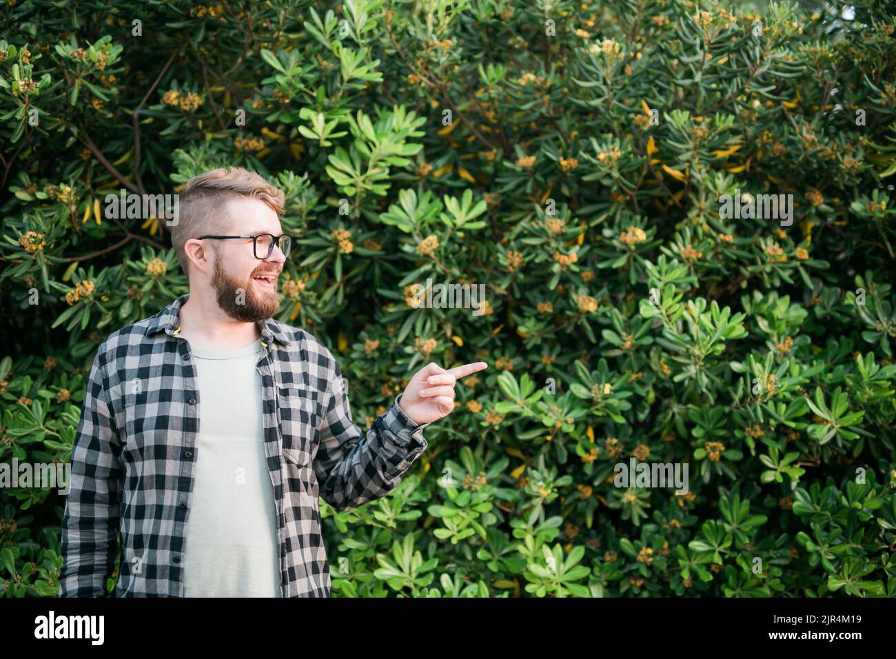 Gros plan portrait beau jeune homme pointe sur le buisson vert à l'extérieur de l'espace de copie et de l'endroit pour la publicité. Banque D'Images
