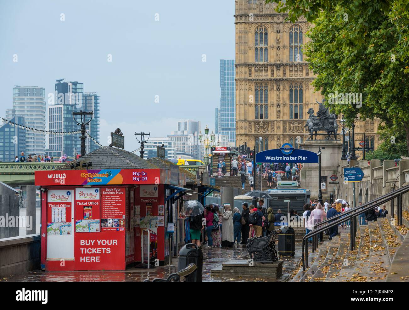 Touristes et touristes aux stands de vente de billets d'excursion lors d'une journée de pluie à Westminster Pier. Londres, Angleterre, Royaume-Uni. Banque D'Images