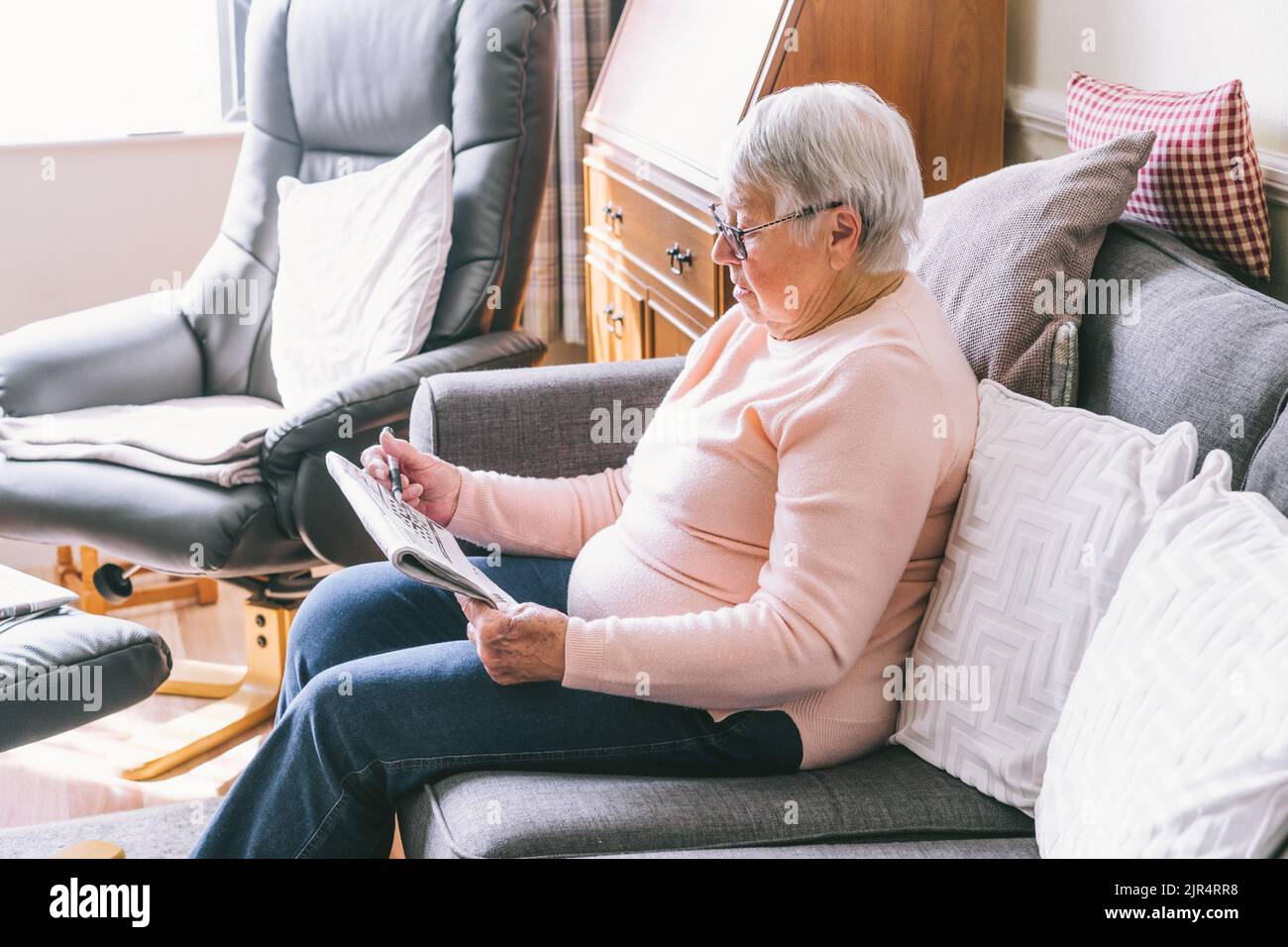 Vieille femme âgée, 80s adultes, grand-mère, faisant des mots croisés dans son salon assis sur le canapé. Passe-temps de retraite pour la mémoire de formation. Alzhe Banque D'Images Vieille femme âgée, 80s adultes, grand-mère, faisant des mots croisés dans son salon assis sur le canapé. Passe-temps de retraite pour la mémoire de formation. Alzhe Banque D'Images