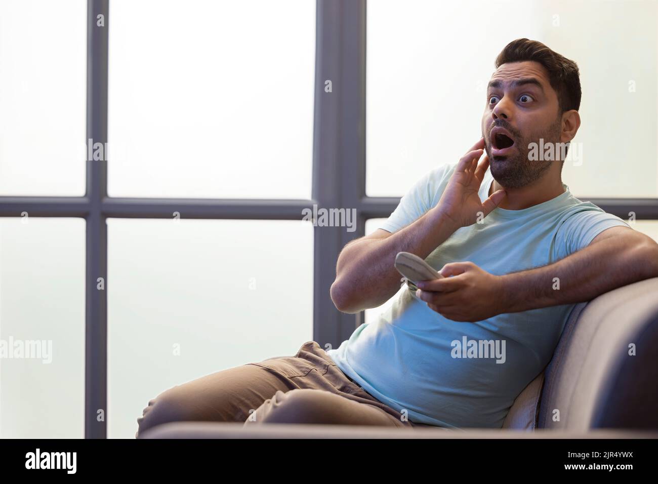 Portrait de jeune homme surpris avec la bouche ouverte tout en regardant la télévision dans le salon Banque D'Images