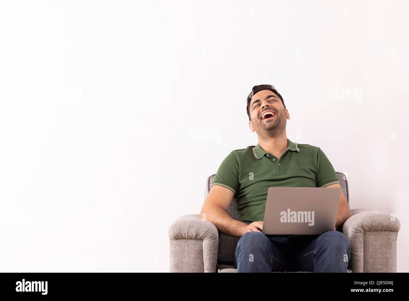 Portrait d'un jeune homme heureux qui rit tout en utilisant un ordinateur portable sur un canapé Banque D'Images