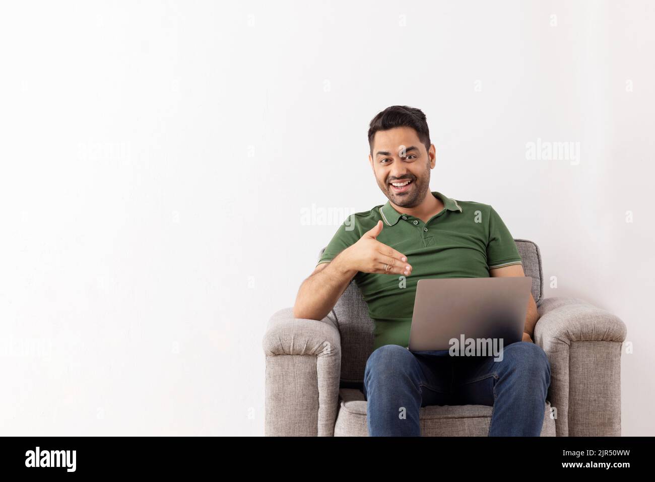 Jeune homme joyeux pointant vers un ordinateur portable tout en étant assis sur un canapé Banque D'Images