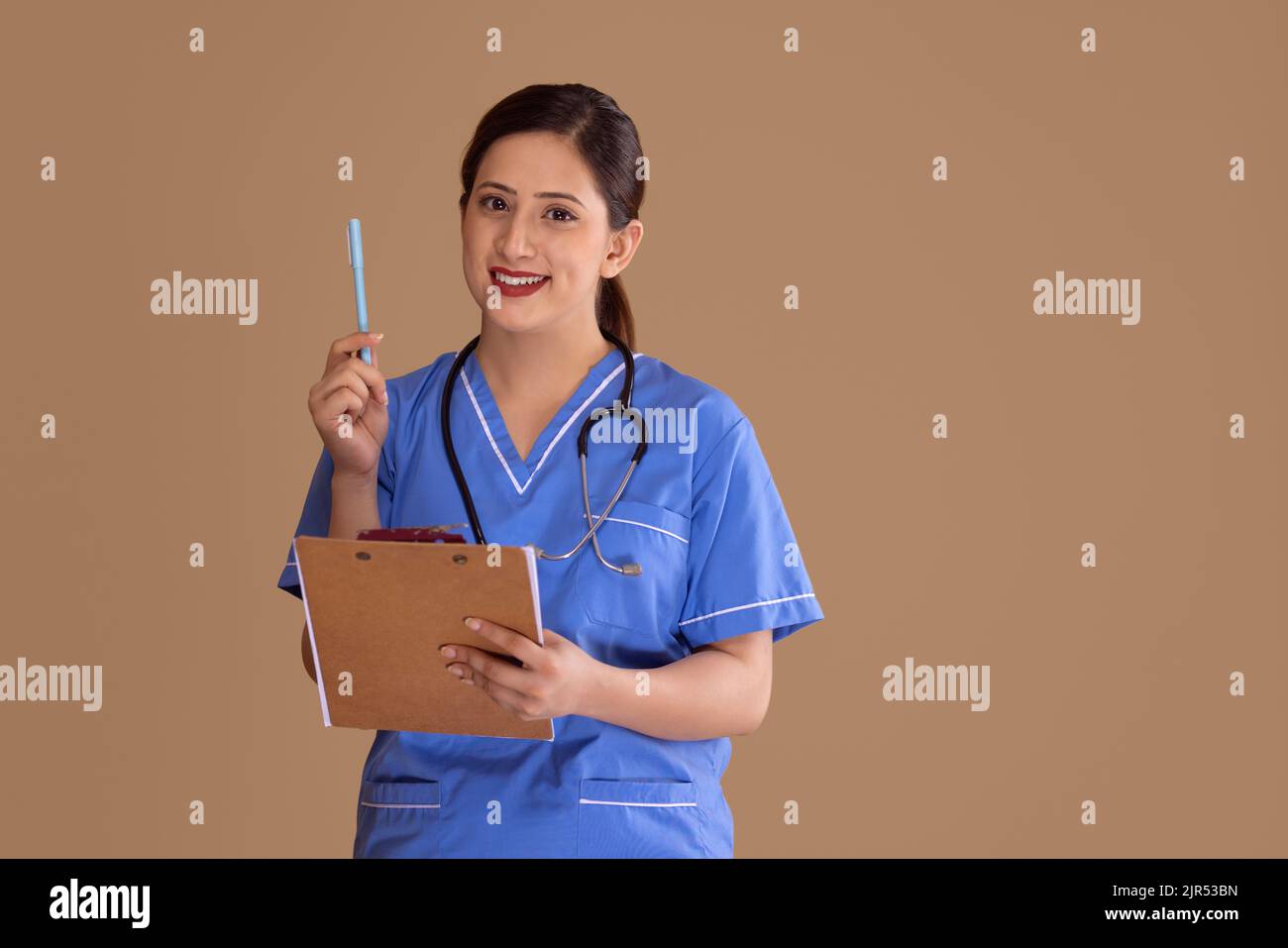 Une jeune infirmière de couleur bleue se frotte avec un stéthoscope autour de son cou, tenant une planchette à pince et un stylo Banque D'Images