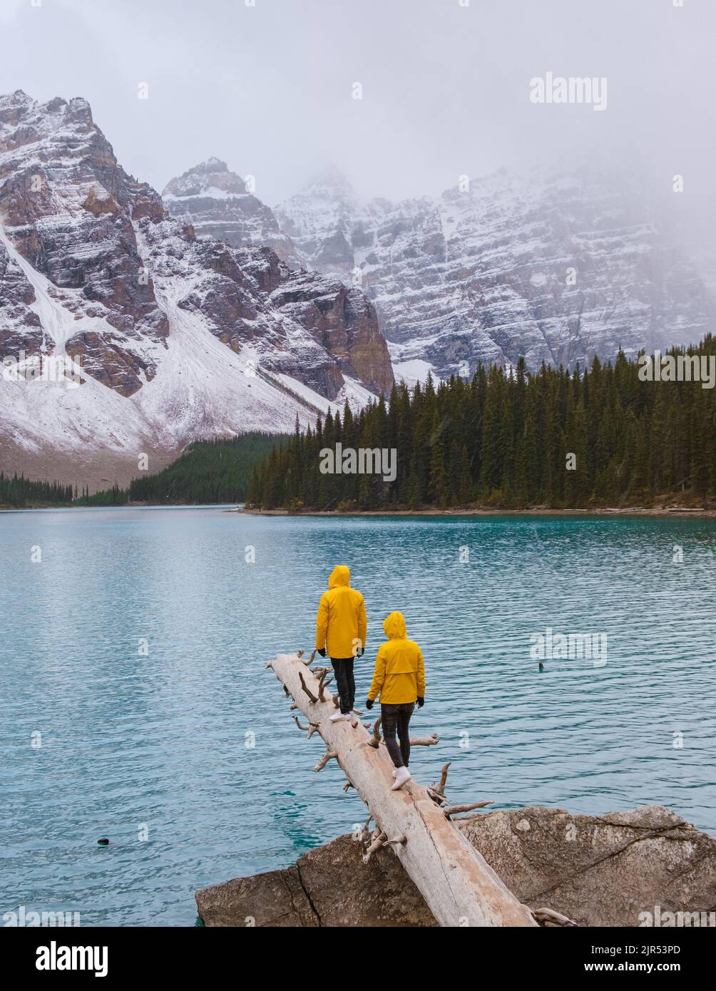 Lac Moraine pendant une journée de neige froide en automne au Canada, de belles eaux turquoise du lac Moraine avec de la neige. Couple d'hommes et de femmes en manteau de pluie jaune pendant la neige Banque D'Images