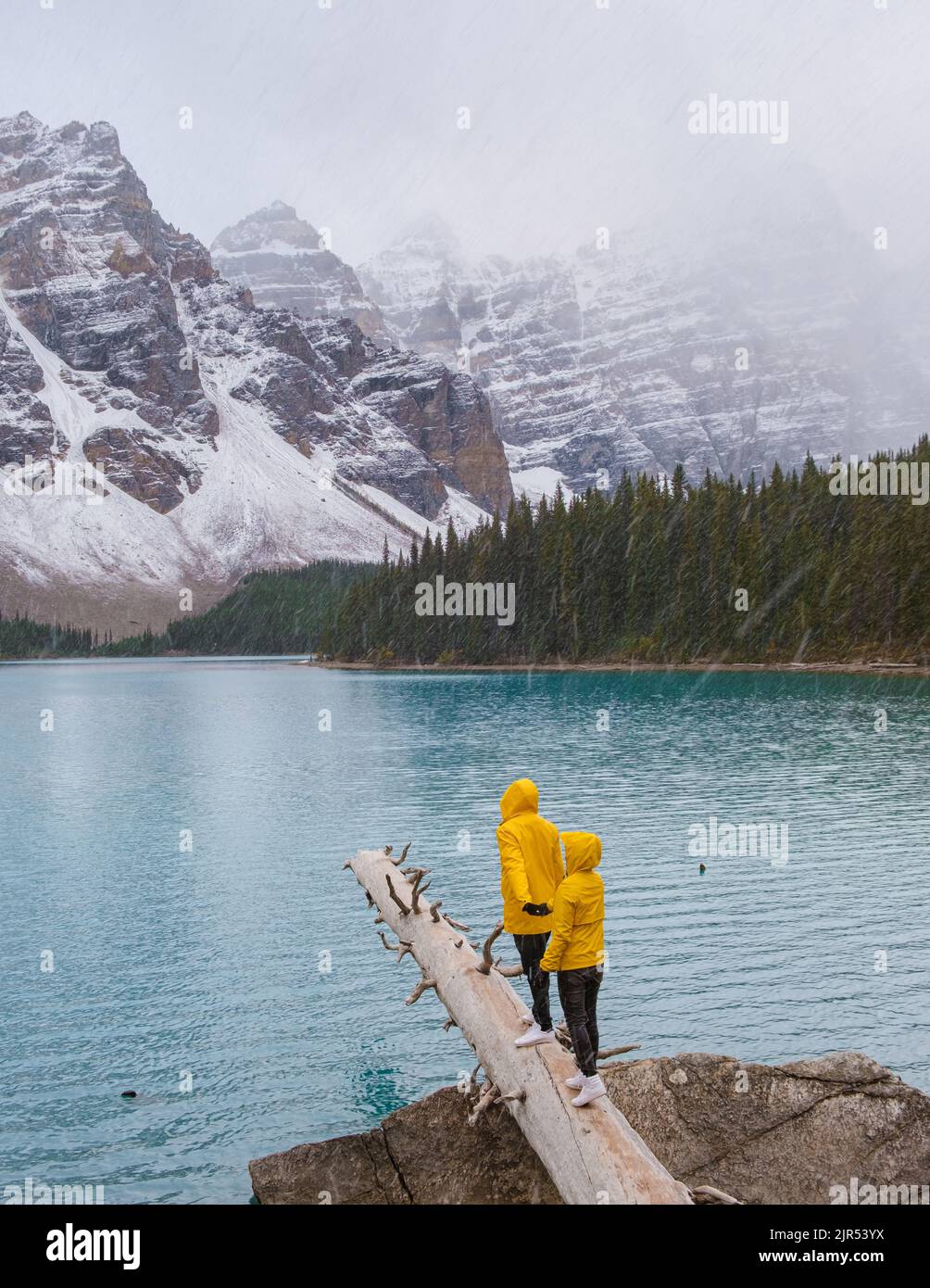 Lac Moraine pendant une journée de neige froide en automne au Canada, de belles eaux turquoise du lac Moraine avec de la neige. Couple d'hommes et de femmes en manteau de pluie jaune pendant la neige Banque D'Images