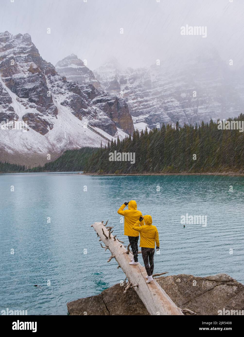 Lac Moraine pendant une journée de neige froide en automne au Canada, de belles eaux turquoise du lac Moraine avec de la neige. Couple d'hommes et de femmes en manteau de pluie jaune pendant la neige Banque D'Images