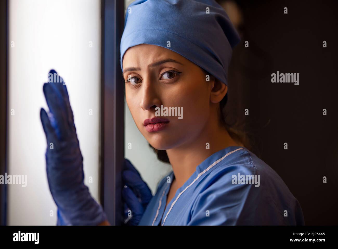 Gros plan d'une jeune infirmière féminine réfléchie debout près de la fenêtre à l'hôpital. Banque D'Images Gros plan d'une jeune infirmière féminine réfléchie debout près de la fenêtre à l'hôpital. Banque D'Images