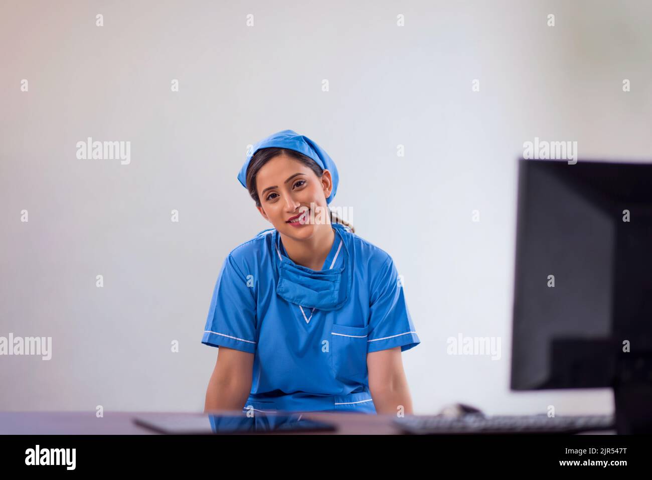 Portrait d'une infirmière heureuse assise au bureau d'ordinateur sur fond blanc Banque D'Images Portrait d'une infirmière heureuse assise au bureau d'ordinateur sur fond blanc Banque D'Images