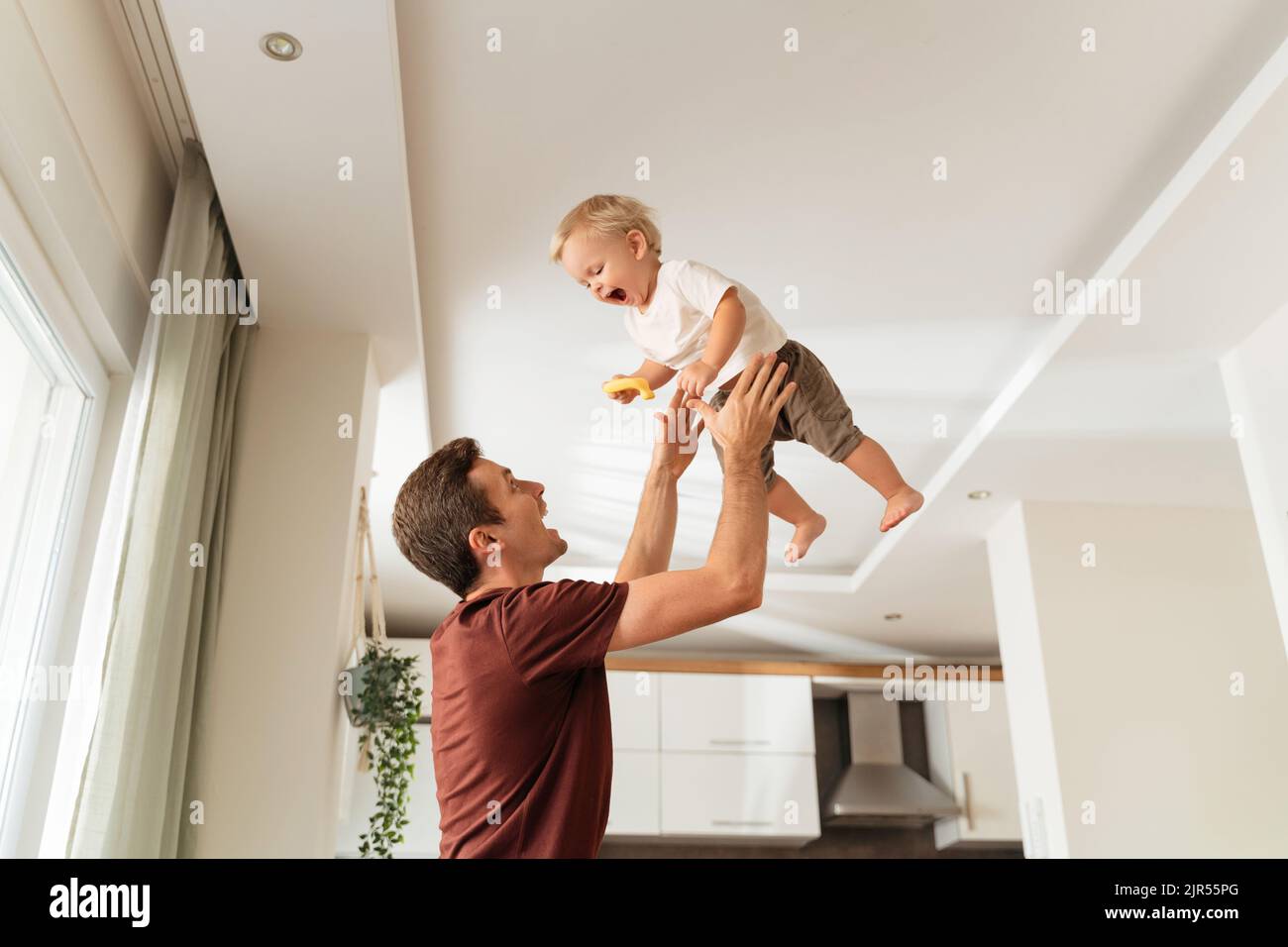 Un jeune père se met à rire et à attraper un bébé, à l'amuser et à s'amuser ensemble après son retour au travail pendant que sa mère prépare un dîner. Jouez activement à la maison Banque D'Images