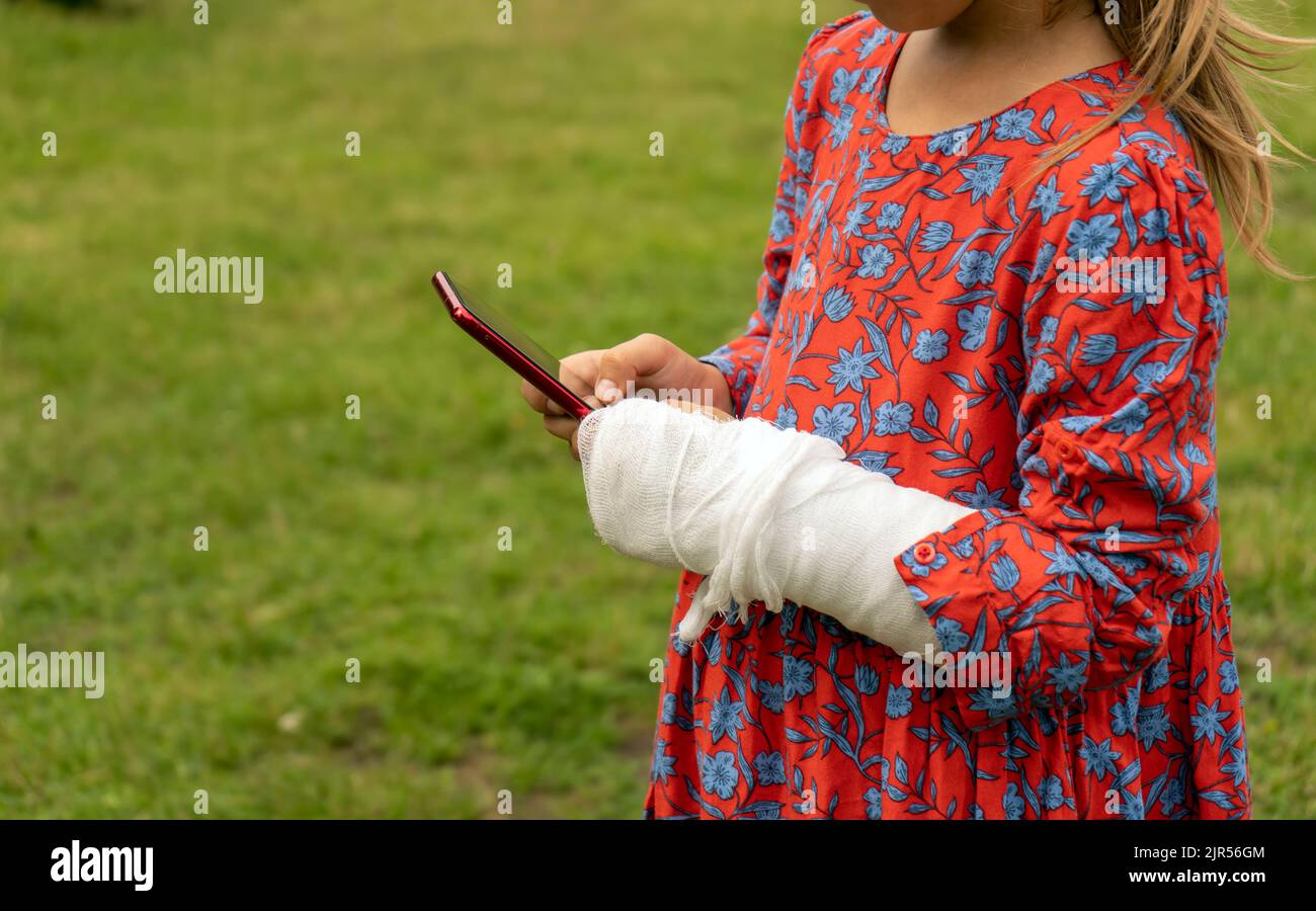 Petite fille avec un casting sur son bras essayant d'utiliser le téléphone Banque D'Images