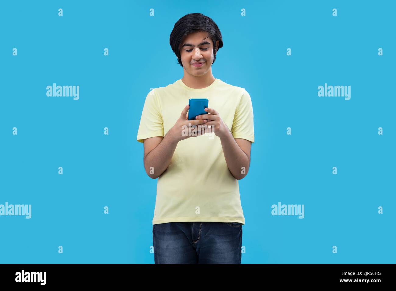 Portrait d'un adolescent heureux à l'aide d'un smartphone tout en se tenant sur fond bleu Banque D'Images