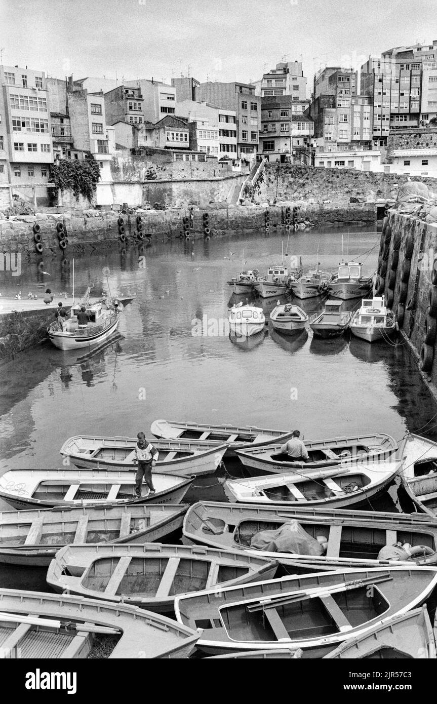 ESPAGNE - Galice - 1970s. Enfants jouant dans les bateaux à rames à Malpica port avec la ville en arrière-plan., Galice, nord-ouest de l'Espagne. Copyright P Banque D'Images