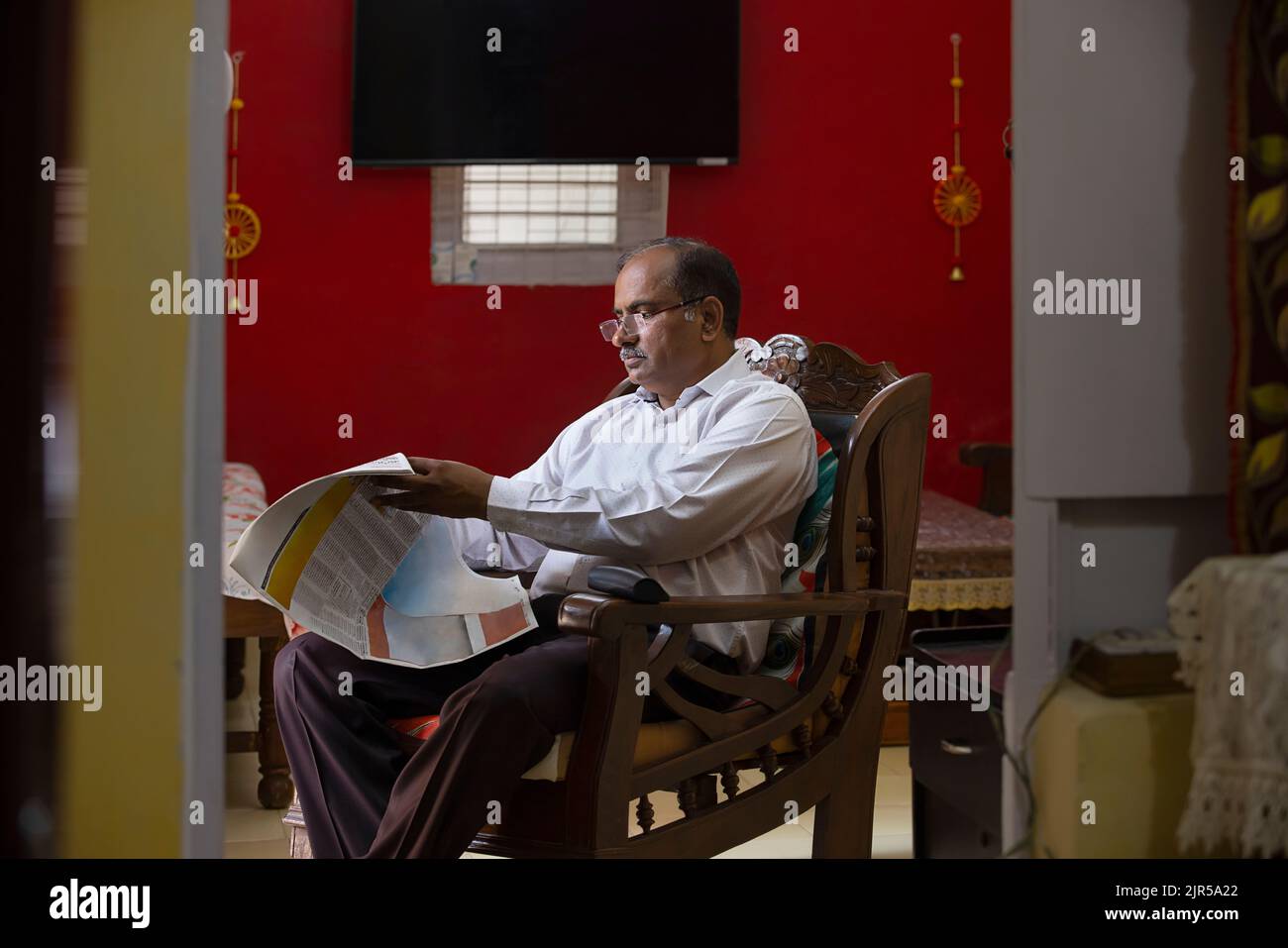 Portrait d'un homme âgé qui lit le journal tout en étant assis sur un fauteuil dans la salle de séjour Banque D'Images