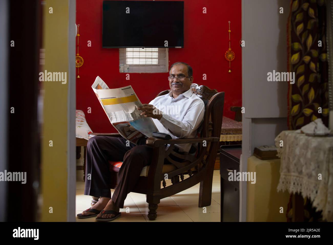 Portrait d'un homme âgé qui lit le journal tout en étant assis sur un fauteuil dans la salle de séjour Banque D'Images