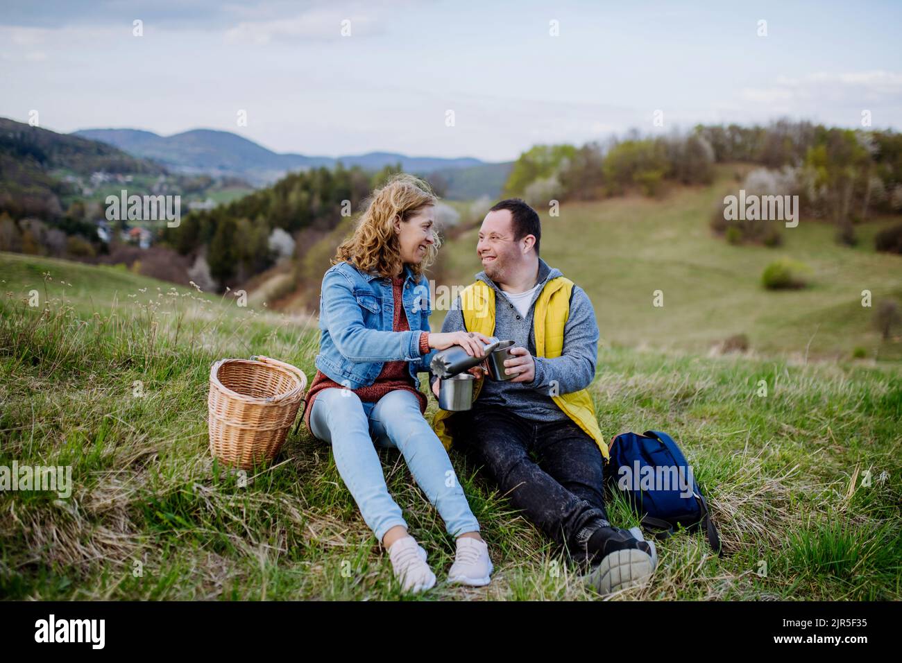 Portrait d'un jeune homme heureux avec le syndrome de Down avec sa mère se reposant dans la nature, assis et buvant du thé. Banque D'Images