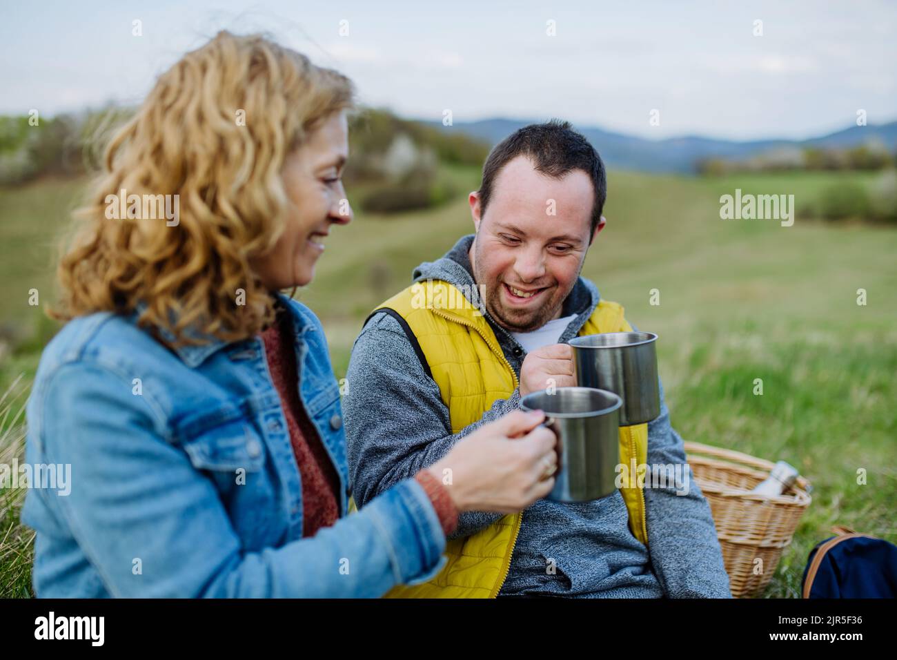 Portrait d'un jeune homme heureux avec le syndrome de Down avec sa mère se reposant dans la nature, assis et buvant du thé. Banque D'Images