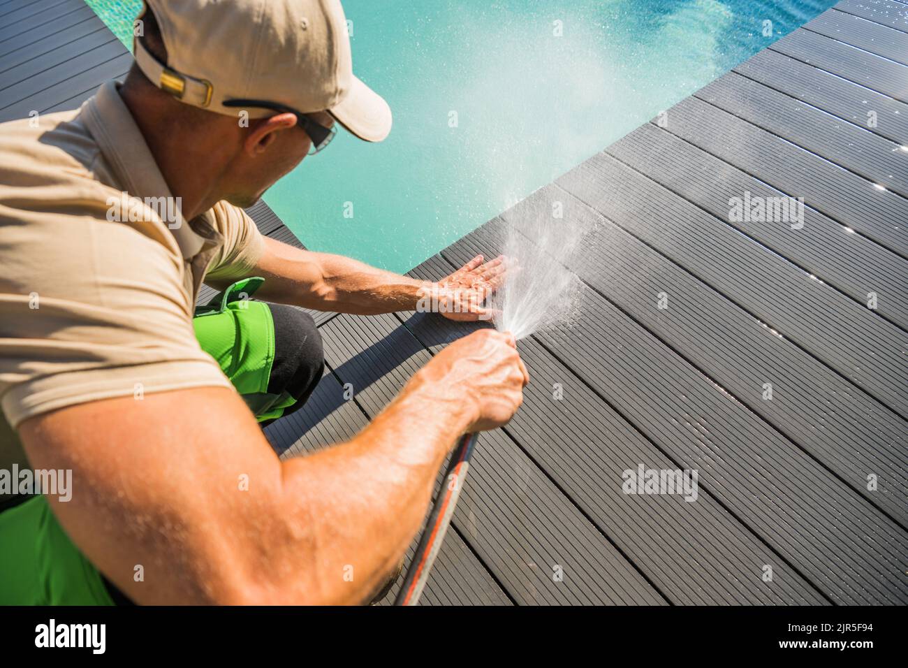 Les hommes caucasiens laver son matériau composite fait la terrasse de piscine à l'aide de tuyau de jardin. Entretien des environs de la piscine. Banque D'Images