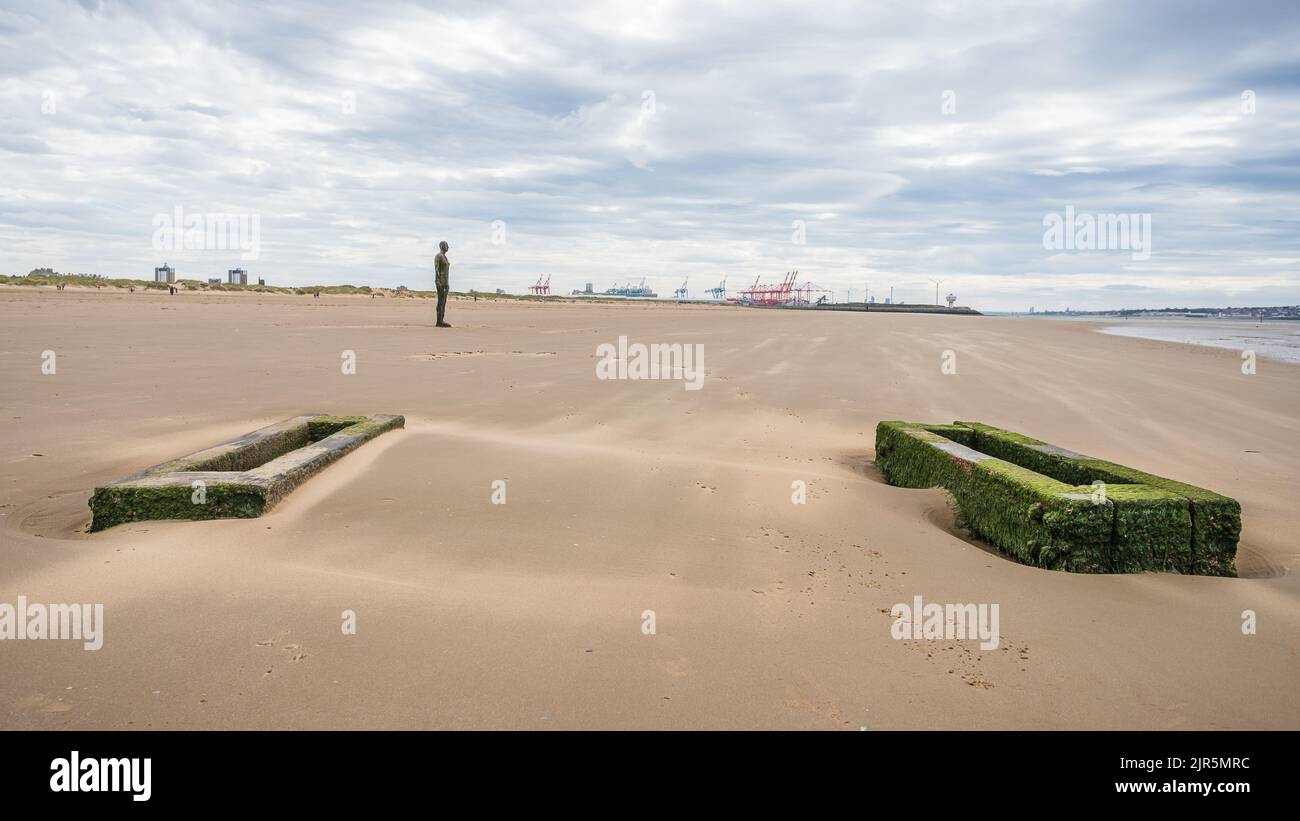 Un homme de fer sur une plage venteuse de Crosby près de Liverpool vu en août 2022 derrière une paire de supports de tuyaux en bois. Banque D'Images