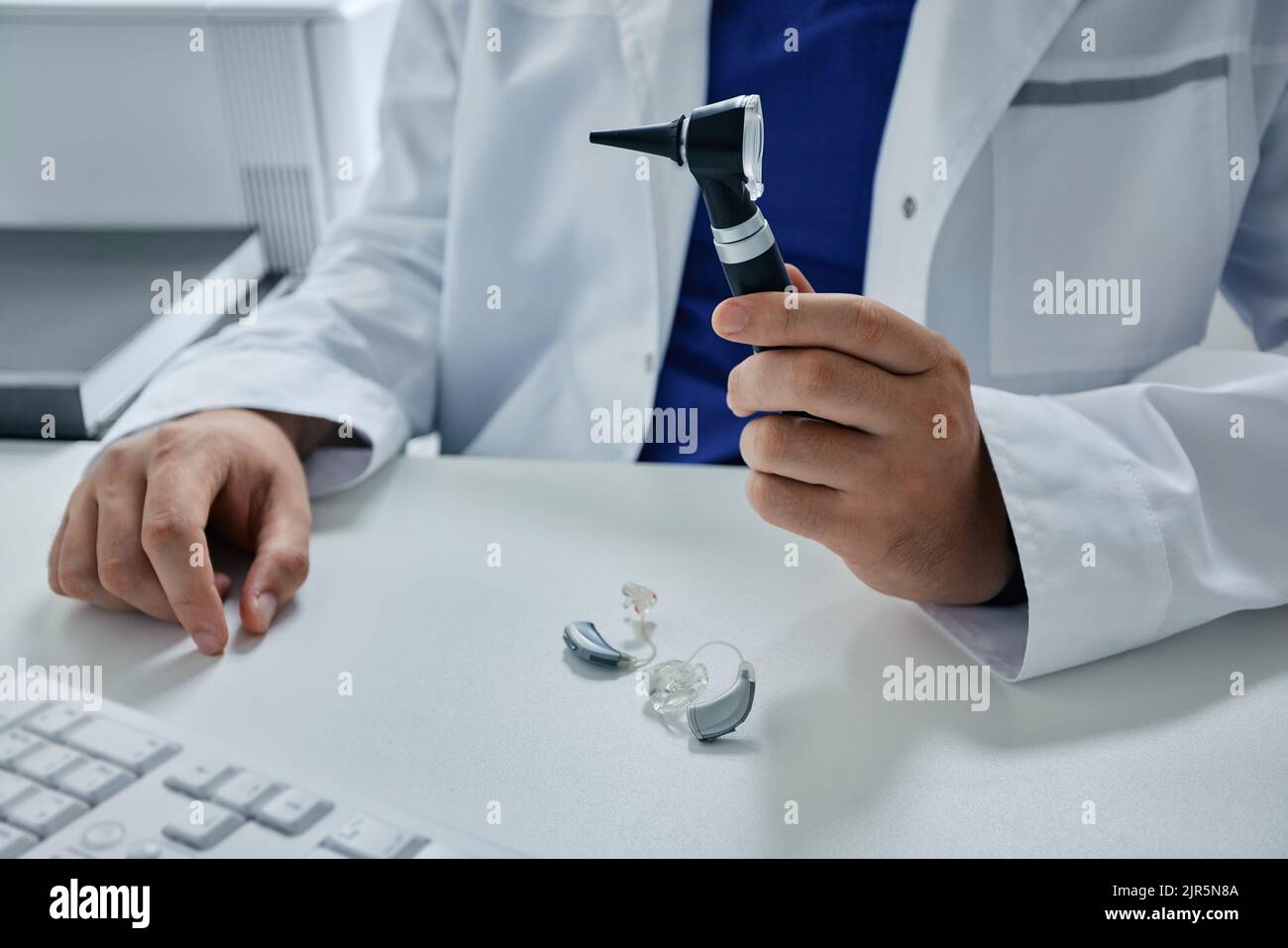 ORL médecin avec otoscope dans les mains assis dans son bureau d'audiologie. Consultation d'audiologistes, traitement de la surdité, sélection de prothèses auditives Banque D'Images