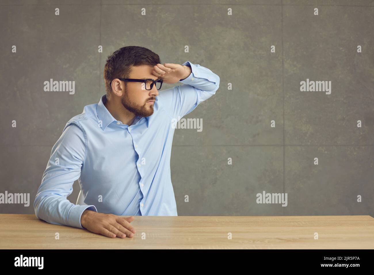 Un homme sérieux est assis à une table et regarde à la distance en tenant sa main au-dessus de sa tête. Banque D'Images