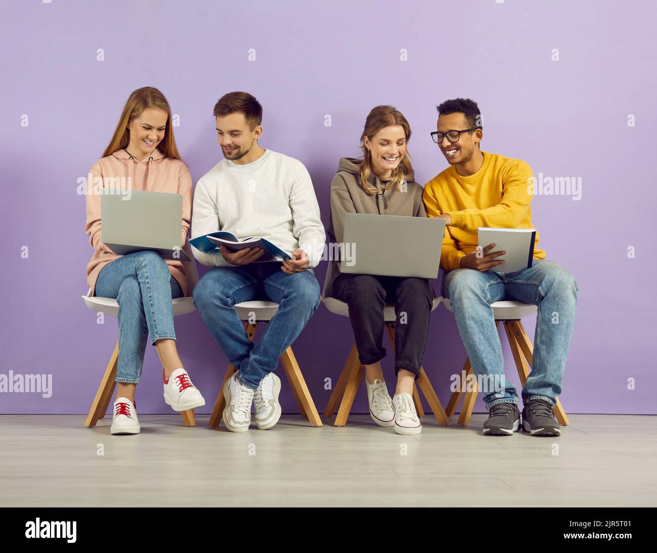 Les étudiants assis en rangée sur fond violet parlent et étudient à l'aide de gadgets et de carnets Banque D'Images