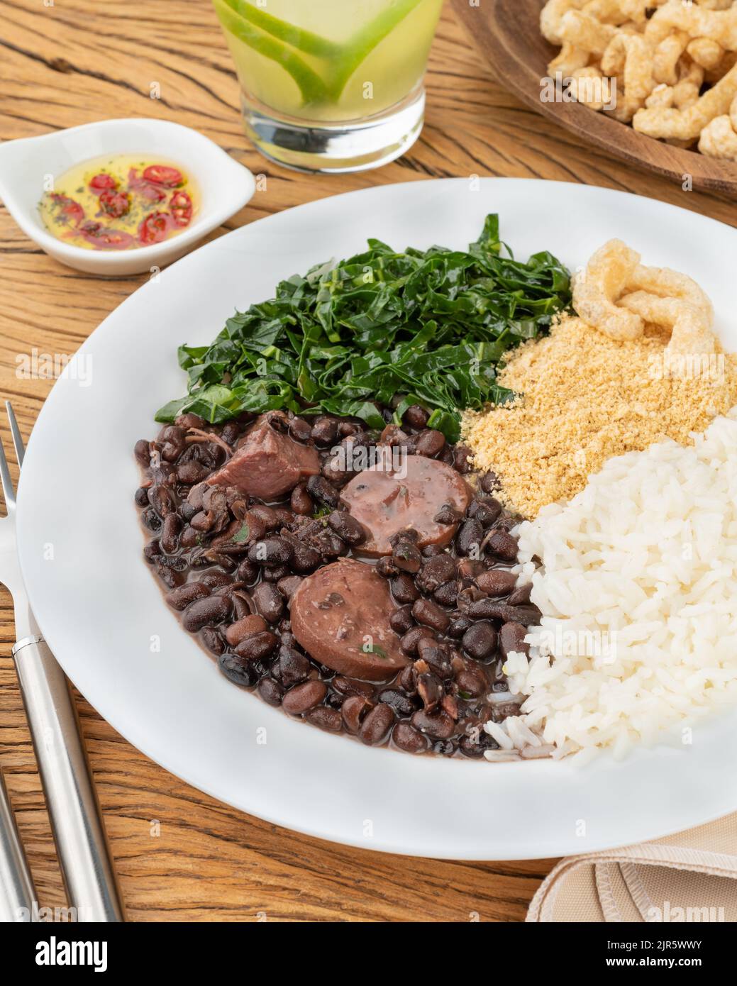 Féijoada brésilienne typique avec riz, poivre, farofa, kale, caipirinha et crépitements. Banque D'Images