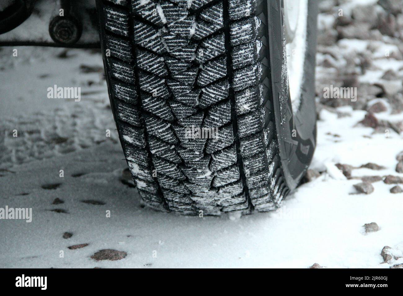 Neige sur un pneu d'hiver, bandes de roulement sur une route en gravier détaillée Banque D'Images