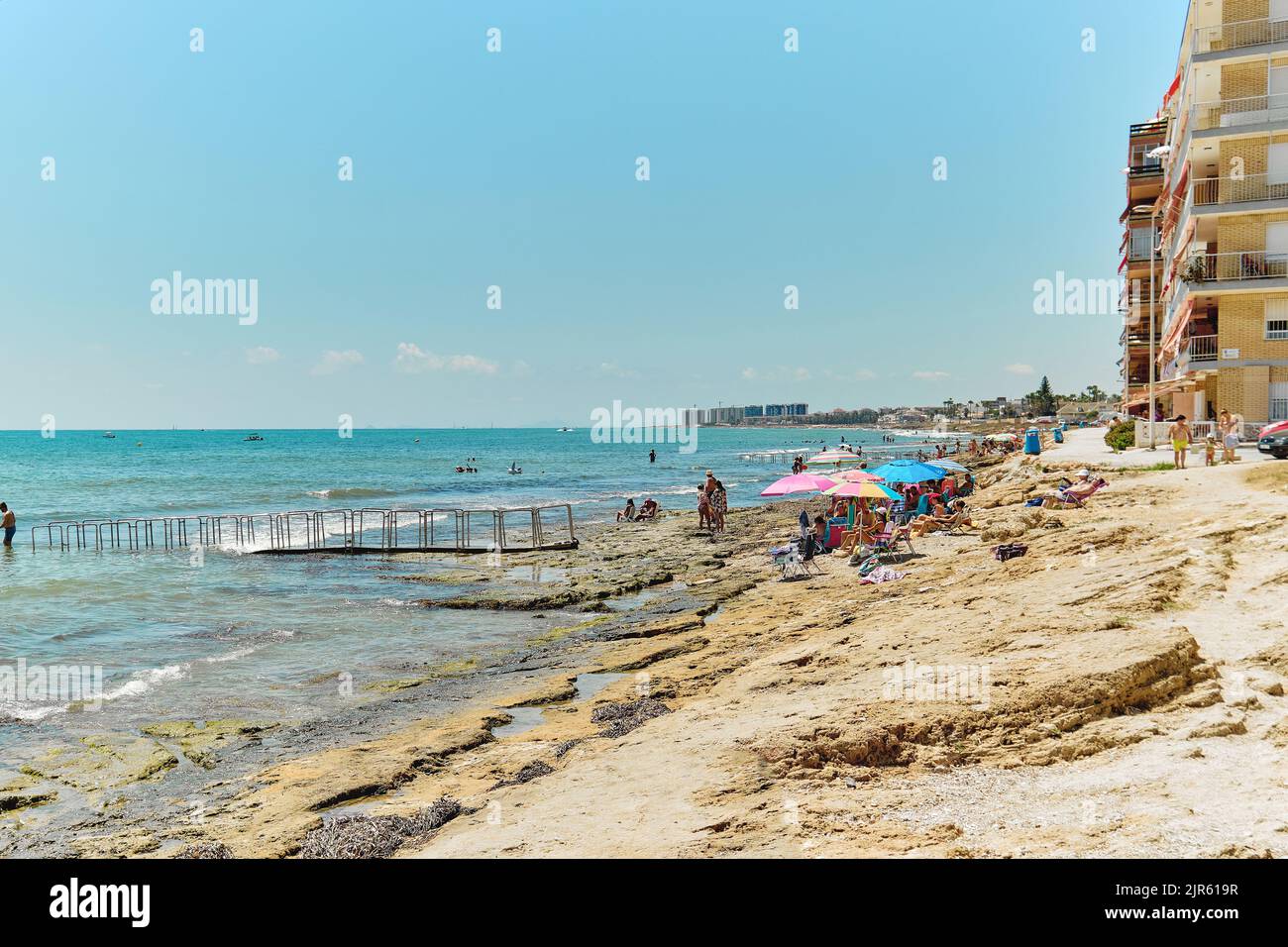 Torrevieja, Espagne - 2 août 2022: Les touristes se bronzer sur la plage rocheuse, profiter de la mer Méditerranée passer des vacances sur la côte sablonneuse. Vacances d'été. Co Banque D'Images