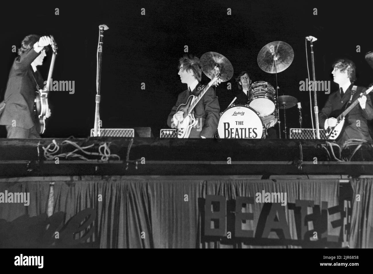 The Beatles sur scène au Gator Bowl à Jacksonville, Floride, sur 11 septembre 1964. L'ouragan Dora avait frappé Jacksonville la veille et des vents violents, qui soufflaient à 45 km/h, ont exigé que les tambours de Ringo Starr soient cloués sur la scène et ont causé le lettrage « Beatles » en carton sur le côté de la scène à finalement être arraché. (ÉTATS-UNIS) Banque D'Images