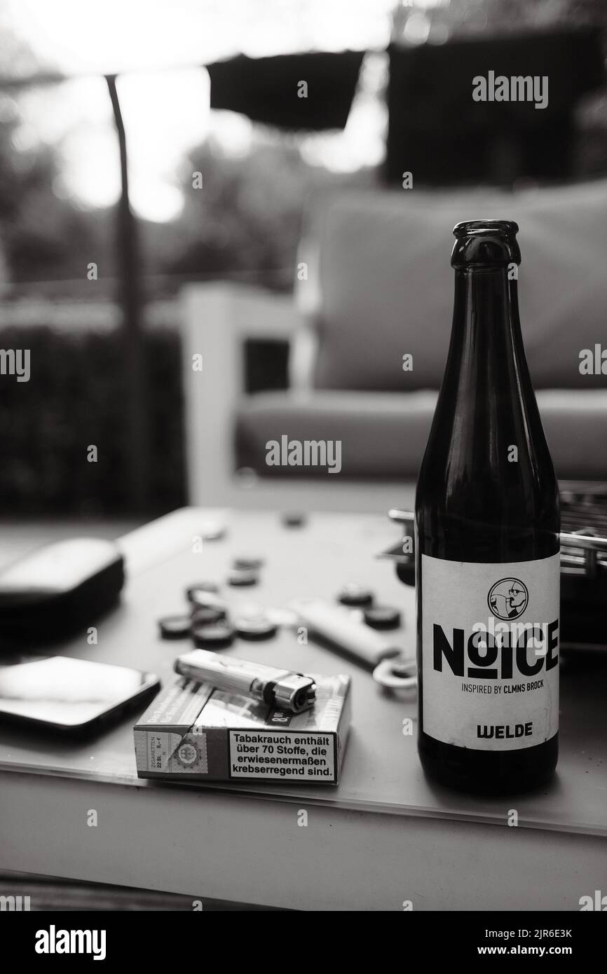 Une photo verticale en niveaux de gris de la bière Noice et un paquet de cigarettes Lucky Strike sur une table de jardin Banque D'Images Une photo verticale en niveaux de gris de la bière Noice et un paquet de cigarettes Lucky Strike sur une table de jardin Banque D'Images